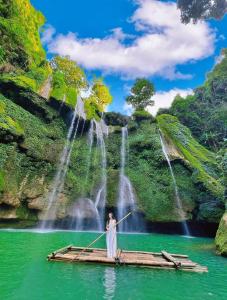 a woman standing on a bamboo raft in a lake in front of waterfall at Happy House Moc Chau in Mộc Châu
