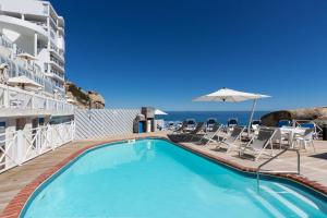 a swimming pool with chairs and an umbrella and the ocean at Modern & Luxurious Seaside Apartment in Cape Town