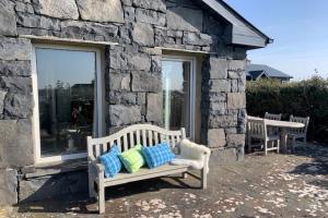 un banco con almohadas sentado fuera de un edificio de piedra en Detached cottage overlooking lake in Connemara, en Ballyconneely