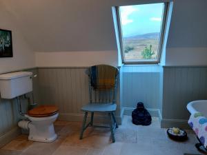 a bathroom with a toilet and a chair and a window at Stone fronted detached cottage just over 2 miles from Mulranny village in Mulranny