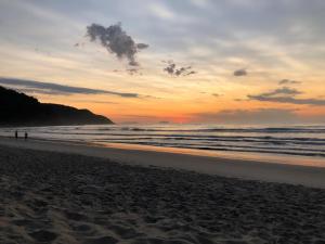 um pôr do sol na praia com pessoas caminhando na areia em Waimea FLATS Itamambuca em Ubatuba