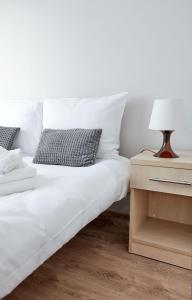 uma cama com lençóis brancos e uma mesa com um candeeiro em Osiedle Zwycięstwa Standard Apartment em Poznań