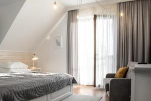 a white bedroom with a bed and a chair at Apartamenty Pod Kominkiem in Rydzewo