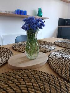 Longère Mille et une roses في Chédigny: مزهرية من الزهور الزرقاء تقف على طاولة خشبية