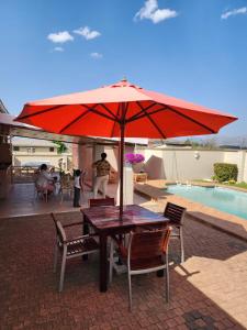 einen Tisch mit einem roten Regenschirm neben einem Pool in der Unterkunft Majestic in Kokstad