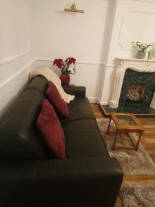 51 Nonsuch Walk, Cheam في Cheam: أريكة سوداء مع وسائد في غرفة المعيشة مع موقد