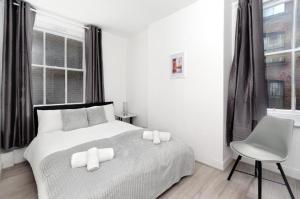 a white bedroom with a bed and a chair at Strand Central Apartments in London