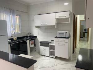 cocina con armarios blancos y microondas en Casa novinha - Praia Grande - Mirim - 3 quadras da Praia Wi-Fi, en Praia Grande