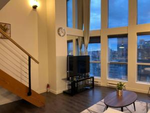 sala de estar con TV y ventanas grandes. en Modern top-floor 1-bedroom loft with free parking, en Vancouver