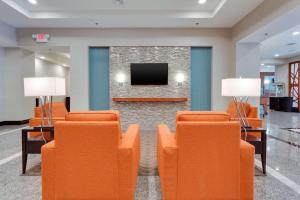 Drury Inn & Suites Fort Myers Airport FGCU في فورت مايرز: غرفة انتظار مع كراسي برتقالية وتلفزيون