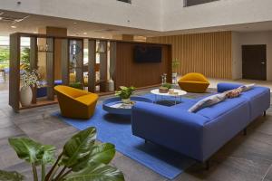 a living room with a blue couch and yellow chairs at City Express Plus by Marriott Cancun Aeropuerto Riviera in Cancún
