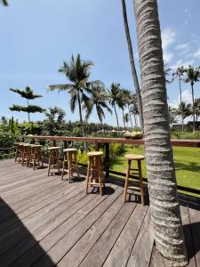 een houten terras met krukken en een palmboom bij Desa Cabins in Balian