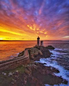 a lighthouse on the shore of the ocean at sunset at Manoir de kerozet - Chambres chez l'habitant in Plouider