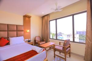 a bedroom with a bed and chairs and a large window at Hotel Sangam in Kanyakumari