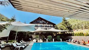 a pool with chairs and umbrellas next to a house at Pensiunea Mai in Păltiniş
