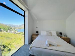 ein Schlafzimmer mit einem Bett und einem großen Fenster in der Unterkunft Stunning Lakeview Holiday House Queenstown in Frankton