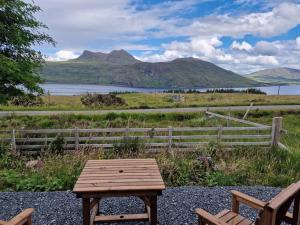 a wooden table sitting on the gravel with a view of a lake at Gorse Gorgeous Glamping Hideaway in Dundonnell