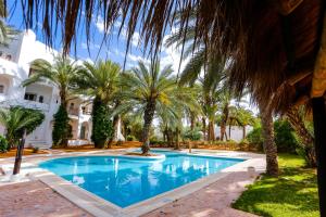 a swimming pool with palm trees in front of a building at Odyssee Resort Thalasso & SPA in Zarzis