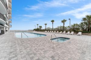 uma piscina com cadeiras brancas e palmeiras em Grand Pointe 401 em Orange Beach