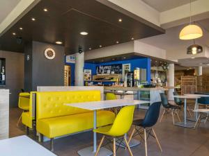 a restaurant with a yellow bench and tables and chairs at Ibis Budget Archamps Porte de Genève in Archamps