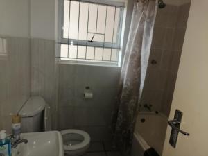a bathroom with a toilet and a sink and a window at 15 uvongo square holiday home in Margate