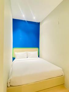 Ruma Ruma Hotel Kenten - Palembang في Sukarami: غرفة نوم مع سرير أبيض مع اللوح الأمامي الأزرق