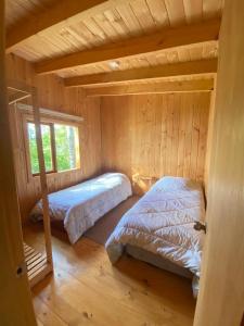 two beds in a log cabin with a window at Cabañas Llifenativo in Futrono