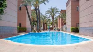 a swimming pool with palm trees and a building at Riad Nezha in Marrakech