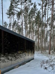 a building in the snow with trees in the background at Mustika Mirror minivilla saunaga in Kärdla