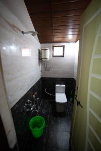 a small bathroom with a toilet and a green bucket at Leo Woods Hampi River view in Hampi