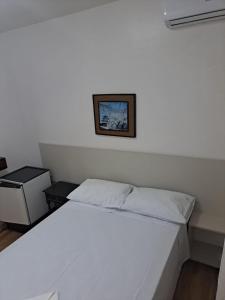 a white bed in a bedroom with a picture on the wall at Vitória Torres Hotel in Torres