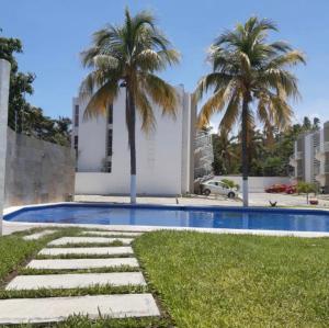 a swimming pool with palm trees in front of a building at Cómodo departamento cerca de Playa Miramar in Manzanillo