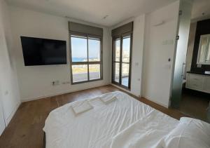 een witte slaapkamer met een bed en een flatscreen-tv bij הקומה ה 16 POOL PENTHAUSE in H̱adera