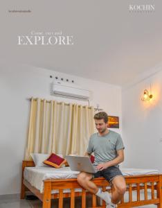 a man sitting on a bed with a laptop at Thanal Homestay in Ernakulam