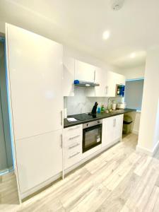 a kitchen with white cabinets and a wooden floor at Comfortable One Bedroom Flat with free Car Park in London in London