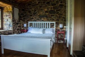 Cama blanca en habitación con pared de piedra en Cabo Do Mundo Casa Rural, en Chantada