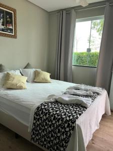 a bedroom with a bed with white sheets and a window at Cantinho da Alegria Suítes in Capitólio