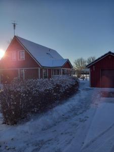 a red barn with a snow covered roof next to a dirt road at Smålandshus in Målilla