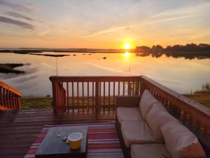 a couch on a deck with a sunset on the water at Marsh House, HOT TUB, Waterfront, KING bed, Close to Lejeune, in Cedar Point