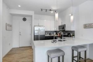 a white kitchen with a counter and two stools at 1BR Oasis in Downtown Tampa w Balcony & City Views in Tampa