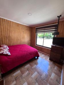 1 dormitorio con cama roja y ventana en Cabañas Vientos del Saltos del laja en Cabrero