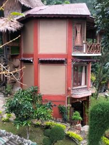 a red house with a balcony in a garden at Junia Guesthouse Bukit Lawang in Bukit Lawang
