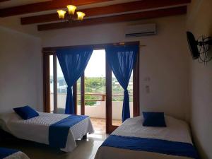 2 Betten in einem Zimmer mit blauen Vorhängen und einem Fenster in der Unterkunft HOSPEDAJE DELFIN AZUL in Puerto Villamil