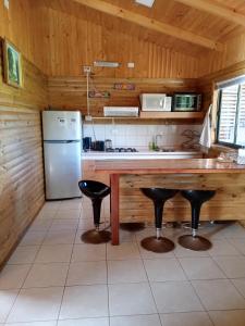 cocina con nevera, mesa y taburetes en Cabaña Don Tito en Buchupureo II, en Buchupureo