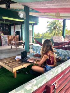 a woman sitting on a couch with a laptop on a table at Beach Break Surf Hostel in Weligama