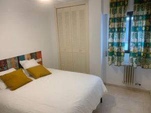 a white bed with yellow pillows in a bedroom at Apartamento, Piccolo Mare, junto centro, vistas Sierra Nevada in Granada