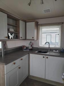a kitchen with white cabinets and a sink and a window at hot tub luxury caravan 23 Lancaster tattershall lakes in Tattershall