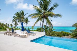 a villa with a swimming pool and palm trees at Pineapple House home in Governorʼs Harbour
