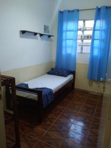 um pequeno quarto com uma cama com cortinas azuis em pousada&Hostel perola mar em Mongaguá