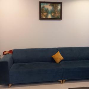 un sofá azul con una almohada amarilla sentada bajo una pintura en لؤلؤ الدرب...ليالي ملكية, en Qarār